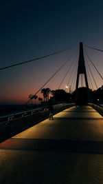 Silhouette people on suspension bridge against sky during sunset
