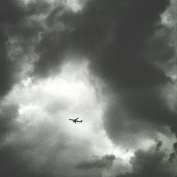 Low angle view of airplane flying against cloudy sky