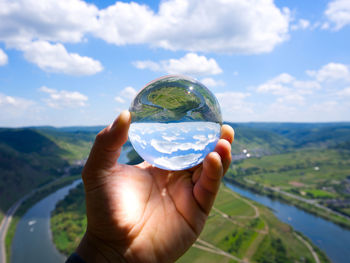 Cropped hand of person holding crystal ball against sky