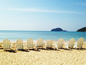 Deck chairs arranged at beach against blue sky during sunny day