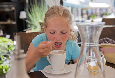 Teenage girl having drink while sitting in cafe