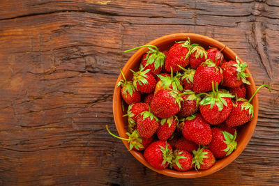 Ripe strawberries in a clay plate on a wooden table. horizontal photo