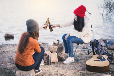 Friends toasting beer at lakeshore during picnic