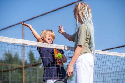 Rear view of young woman with arms raised standing against chainlink fence