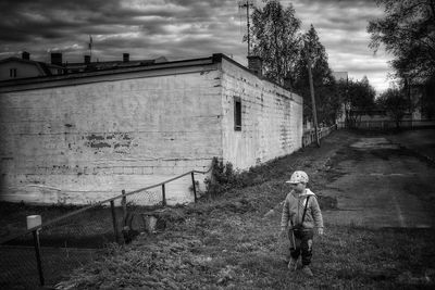 Boy walking by house against sky