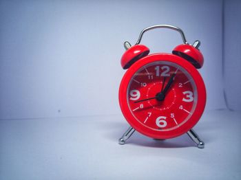 Close-up of red clock on table against wall
