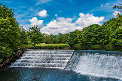 Scenic view of waterfall by river against sky