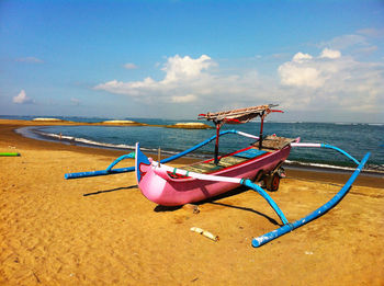Outrigger boat moored at beach against blue sky