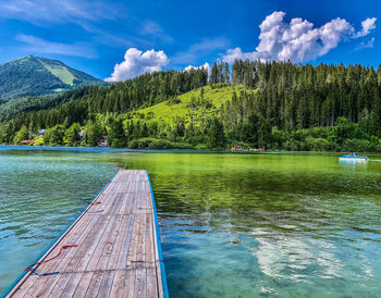 Scenic dock view of lake in forest against sky between hills of alps mountain