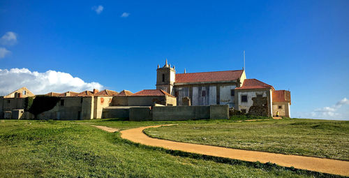 Footpath on grassy field leading towards houses against sky