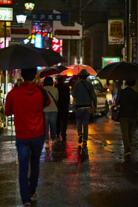 Rear view of people walking on city street during rainy season during night