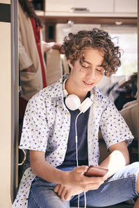 Teenage boy with headphones using mobile phone in camper van