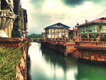 Old tourist resort by river against cloudy sky