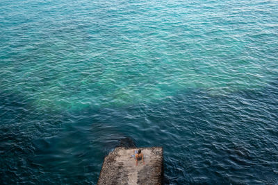 High angle view of person sitting at cliff in front of ocean 