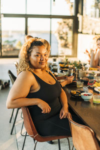 Portrait of smiling plus size woman sitting on chair with breakfast at dining table