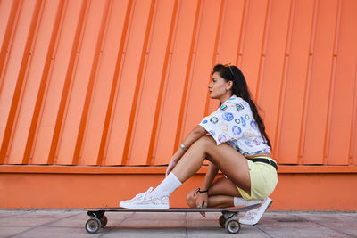 Full length portrait of woman sitting against orange wall