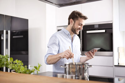Young man looking at with mini tablet while cooking