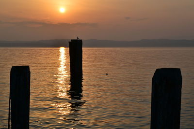 Silhouette wooden posts in sea against sky during sunset