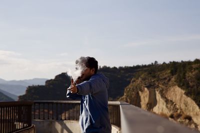 Side view of young man standing on mountain against sky