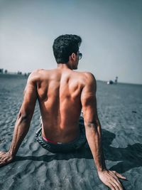 Rear view of shirtless man sitting on sea shore