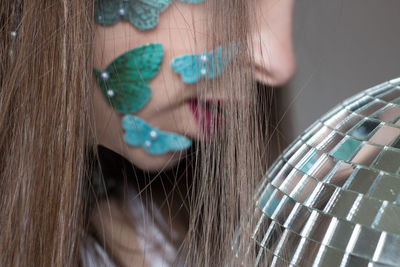 Close-up of woman wearing artificial butterflies on cheek by disco ball