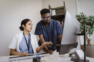 Doctor explaining young male colleague over desktop pc in clinic