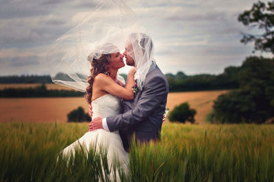 Bride and groom embracing while standing on grassy field