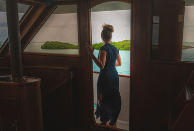 Rear view of woman looking through window at home