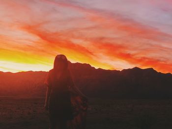 Silhouette woman standing on mountain against orange sky