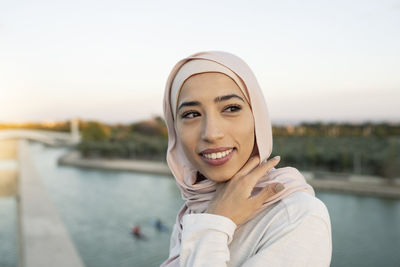 Portrait of cheerful arab female and looking into distance while standing on waterfront with fence near river