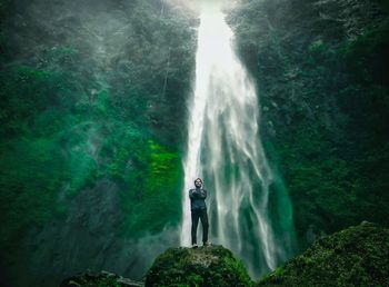Man standing against waterfall in forest