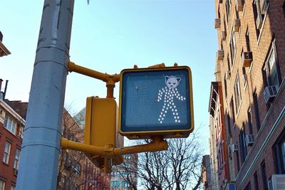 Low angle view of animal sticker on pedestrian crossing sign against sky