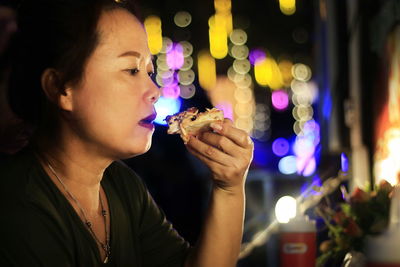 Woman eating food against illuminated lights at restaurant