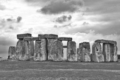 Stonehenge ruins on field against cloudy sky