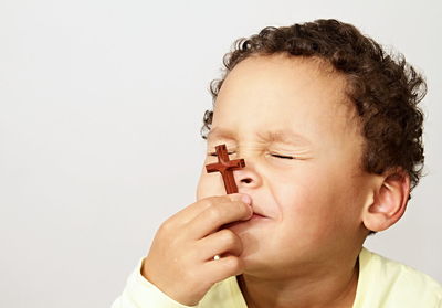 Cute boy holding cross praying against white background