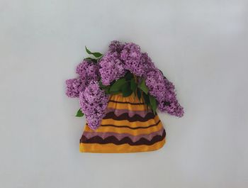 Close-up of purple flowers in knitted habdbag against white wall