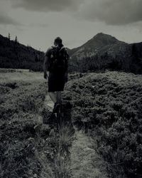 Rear view of man walking on mountain against sky