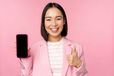 Portrait of young woman holding mobile phone against pink background