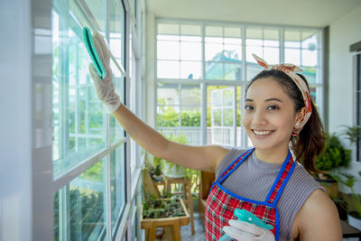 Portrait of smiling young woman cleaning window