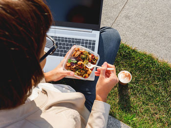 Woman sits on park bench with laptop and lunch box. healthy bowl with vegetables. healthy nutrition.