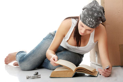 Young woman sitting on book against white background