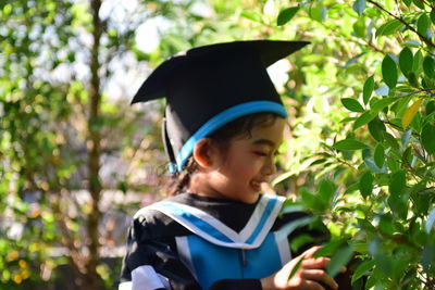 Smiling girl wearing graduation gown and mortarboard by plants