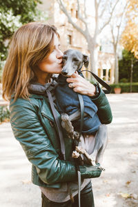 Cute young woman hugging and kissing her italian greyhound small breed of dog.  outdoor photo