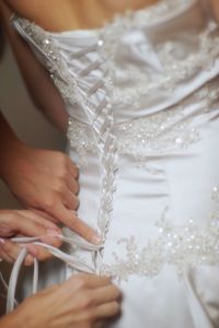 Cropped hands of bridesmaid adjusting wedding dress of bride