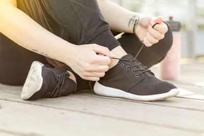 Low section of woman tying shoelace while sitting on floorboard