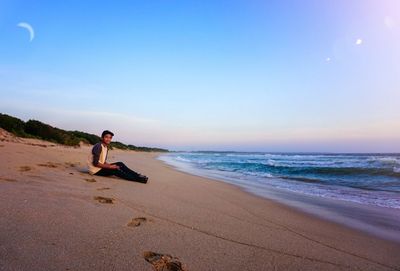 Full length of man sitting on shore at beach