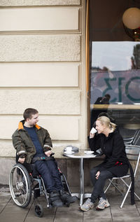 Female caretaker and disabled man having coffee at sidewalk cafe