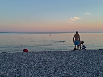 Men on beach against sky during sunset