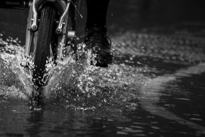 Low section of person cycling and splashing water in puddle