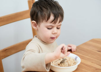 Little boy eating oatmeal for breakfast in the kitchen